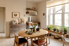 a dining room table with chairs and potted plants on the table in front of large windows