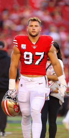 a football player is walking on the field with his helmet in hand and other people behind him