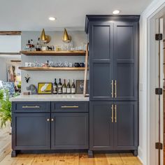 a kitchen with gray cabinets and gold handles on the countertop, along with shelves filled with wine bottles