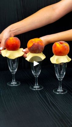 three wine glasses with peaches in them being held by someone's hand over the top