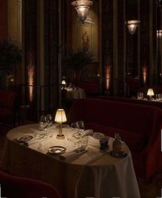 a dimly lit dining room with red chairs and white table cloth on the tables in front of two chandeliers