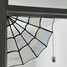 a stained glass window with a spider web hanging from it's side, in front of a white wall