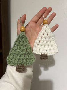 two crocheted christmas trees are being held up by someone's hand,