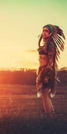 a native american woman standing in a field at sunset