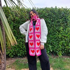 a woman standing in front of a hedge wearing a pink scarf with hearts on it