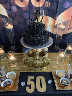 a black cake sitting on top of a table next to some glasses and silverware