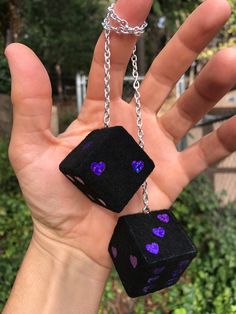 a hand holding two black dices with purple hearts on them