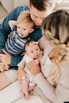 a man and woman holding two babys while sitting on a couch in the living room