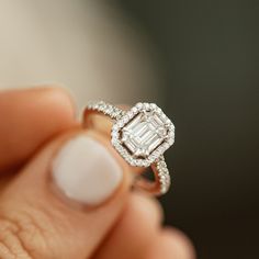 a woman's hand holding an engagement ring with a diamond in the center and two rows of diamonds on each band