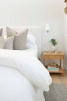 a bed with white linens and pillows in a bedroom next to a wooden night stand