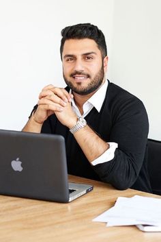 a man sitting at a table in front of a laptop computer with an apple logo on it