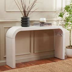 a white console table with a plant and books on the top, in front of a beige wall