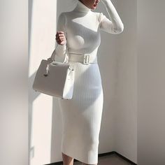 a woman wearing a white dress and carrying a white handbag while standing next to a window