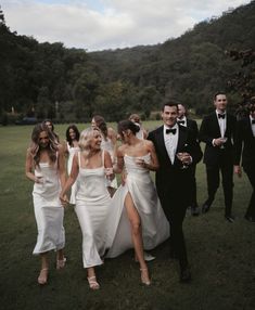 a group of people dressed in formal wear walking through the grass with one woman wearing a white dress