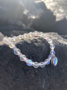 a bracelet with white glass beads and a silver beaded charm sits on top of a rock