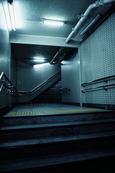 an empty subway station with stairs leading up to the exit door and lights on either side