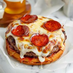 a cheeseburger with pepperoni on it is sitting on wax paper next to a glass of beer