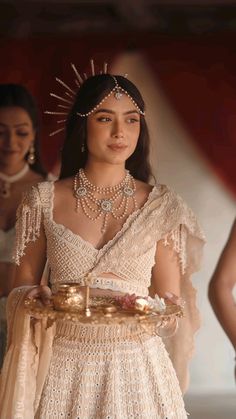 a woman in a white dress and tiara holding a tray with gold dishes on it