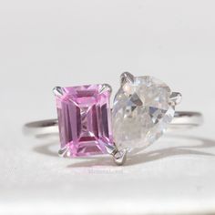 an engagement ring with two pink and white stones on top of each other, sitting on a table