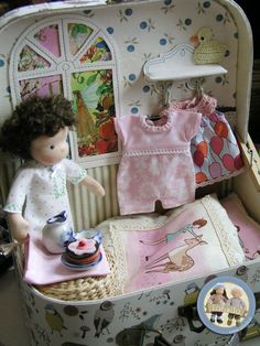 a doll in a suitcase with clothes on the shelf and other items around it,