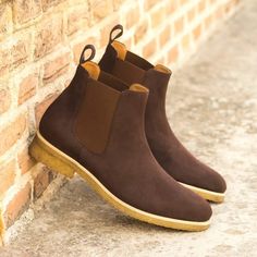 a pair of brown suede boots sitting on the side of a bricked wall