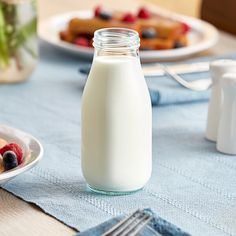 a bottle of milk sitting on top of a table next to plates of food and utensils