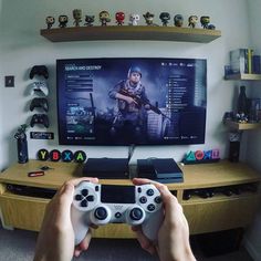 a person holding a video game controller in front of a flat screen tv on top of a wooden entertainment center