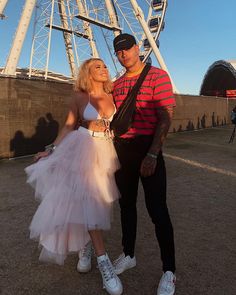 a man and woman standing next to each other in front of a large ferris wheel