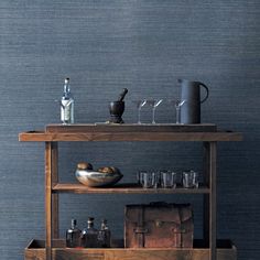 a bar cart with bottles and glasses on it in front of a wallpapered blue background