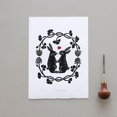 a pair of rabbits in a floral frame on white paper next to a wooden spoon