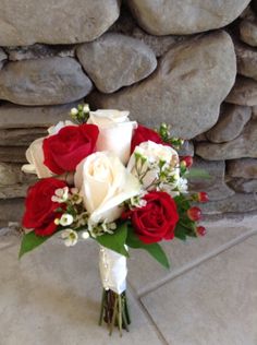 a bridal bouquet with red and white flowers in front of a stone wall on the floor