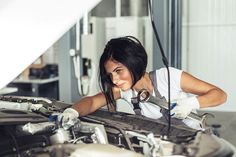 a woman in white shirt working on an engine with wrench at the end of it