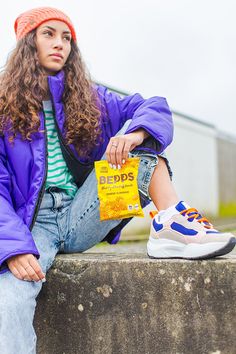 a young woman sitting on top of a cement wall next to a yellow bag and blue jacket