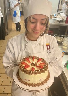 a woman in a chef's outfit holding a cake with strawberries on it