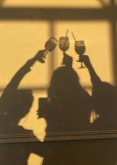 two people holding up wine glasses in front of a window with the sun shining through them