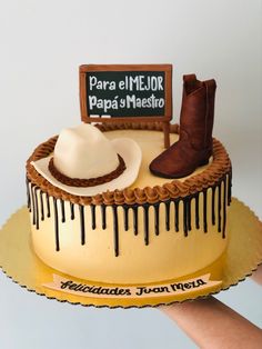 a hand holding a cake decorated with cowboy boots and a sign that says para el emelidor papa y'masito