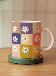 a colorful coffee cup sitting on top of a wooden table next to a vase with flowers