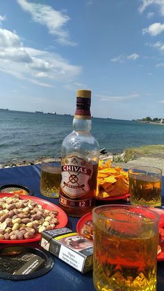 a bottle of alcohol and some food on a table near the water with other foods