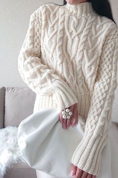 a woman is wearing a white sweater and holding a purse in her hand while sitting on a couch