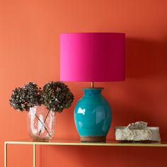 a blue vase sitting on top of a table next to a pink lamp and rocks