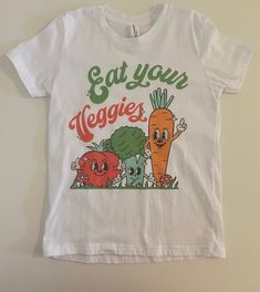 Our new Eat Your Veggies outfit is the outfit of spring! Snag a tee in Black or white, and even add a bottom! Available in adult tees as well! All styles of clothing will be the all over veggie print. Tees will have the graphic. Lounge tees and tanks are the all over print.  Sizing (Message Sizes): Graphic Tees: Babies+Toddlers(6/12M, 12/18M, 2T-5T), Kids (S-XL), and Adult (S-2X Unisex). Care:  To extend the wear of your item, it is recommended to use a gentle wash and tumble dry. If possible, hang-drying is always best for handmade items! Tees should be washed inside out and then hang dried.  Fabric Contents*: Double Brushed Polyester Material - 96% Polyester/4% Lycra Pullovers and Tees will be a thick DBP.  Graphic Tee is a Bella canvas tee.  Turn Around Time (TAT) and Shipping: Current Fun White T-shirt, Organic White Graphic Print Tops, Organic White T-shirt For Summer, Organic White Crew Neck Tops, Funny White T-shirt For Spring, Playful Cotton T-shirt With Front Print, Organic White Short Sleeve Tops, White Funny Text T-shirt For Spring, Spring Organic White T-shirt