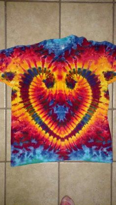 a tie - dyed shirt with a heart on it sitting on a tile floor next to a person's foot