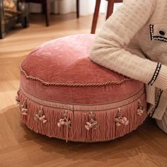 a woman sitting on top of a pink poufle covered ottoman in a living room