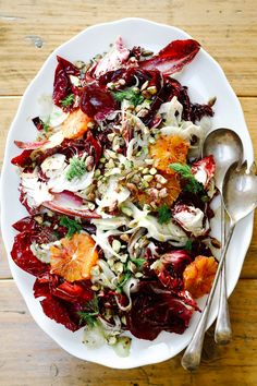 a white plate topped with lots of food on top of a wooden table next to two spoons