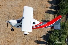 a small red and white airplane flying over a field