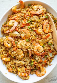 a white bowl filled with rice and shrimp next to a wooden spoon on top of a table