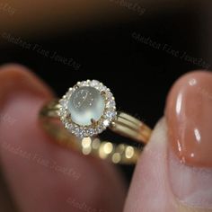 a close up of a person's hand holding a ring with a white stone