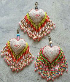 two heart shaped beaded earrings with tassels hanging from the sides on a gray surface