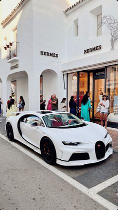 a white bugatti parked in front of a building with people standing around it