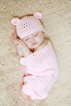 a baby sleeping on top of a blanket wearing a pink knitted hat and sweater